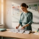 Nederlandse basisschoollerares rangschikt curriculumkaarten op een houten bureau, kleurrijke leerdoelenborden zichtbaar op het whiteboard achter haar.