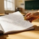 Leraar plakt gouden ster in notitieboek van leerling op houten schoolbank, warm zonlicht door klaslokaalramen.